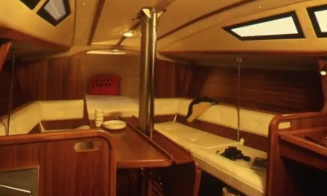 Intérieur chaleureux d'un voilier, avec banquettes en cuir crème, boiseries sombres et hublots. Le **selection 37 interieur** offre un espace confortable pour la vie à bord.