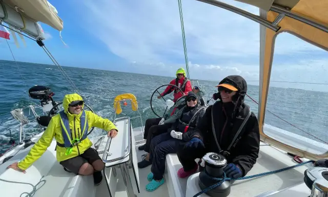 Équipage souriant sur un voilier, profitant de la navigation. Personne n'a besoin d'écoper, la mer est calme.