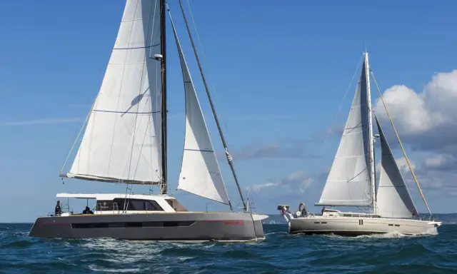 Deux voiliers naviguent sur une mer bleue. L'un est un catamaran gris moderne, l'autre un voilier blanc classique. Une belle journée pour déguster un voilier fruit de mer.