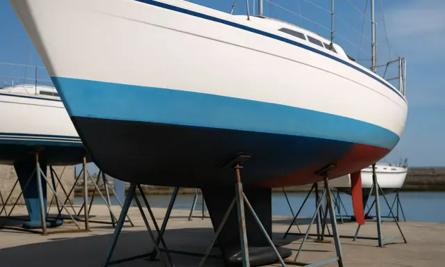 Vue rapprochée de la coque d'un voilier blanc avec une bande bleue et une bande rouge. Le choix couleur coque bateau est important pour l'esthétique.