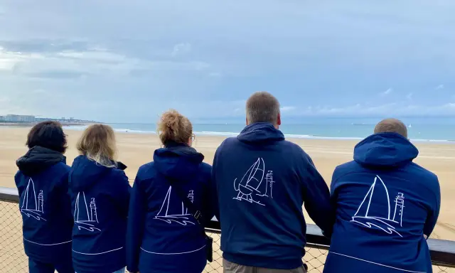 Cinq personnes portent des vestes bleues avec des voiliers dessinés. Benoit Marie et ses amis admirent la mer.