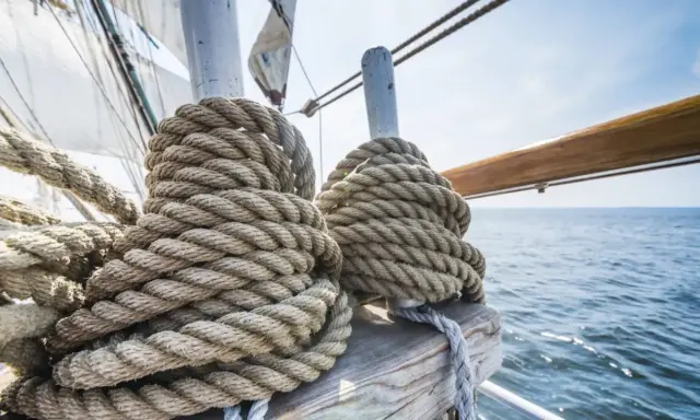 Gros cordages enroulés sur des taquets, prêts pour l'aventure. La proue du bateau fend les flots bleus sous un ciel clair.