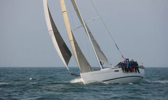 Équipage sur un voilier blanc, le foc et le génois gonflés par le vent, naviguant sur une mer agitée.