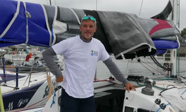 Gildas Mahé, skipper, pose sur son voilier, prêt pour une nouvelle aventure maritime.