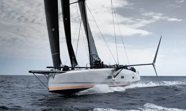 Le voilier Baltic 111 Raven fend les vagues, ses voiles noires gonflées par le vent.