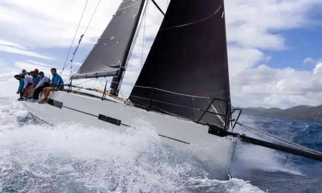 Équipage sur un voilier blanc, gery trentesaux, naviguant sur une mer agitée sous un ciel nuageux.