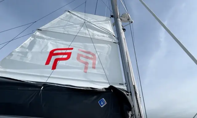 Voile blanche avec logo rouge, prête à naviguer à la voile sous un ciel bleu.