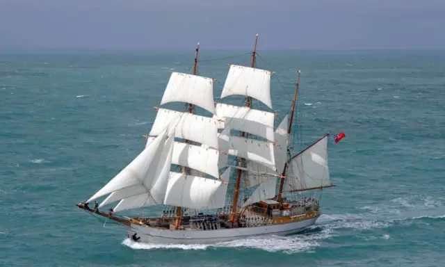 Majestueux voilier 3 mats, ses voiles blanches gonflées par le vent, navigue sur une mer agitée.