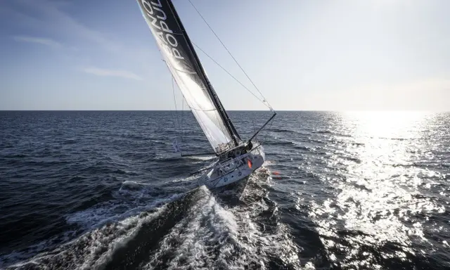 Voilier Banque Populaire naviguant au soleil, l'eau éclabousse le long du babord tribord.