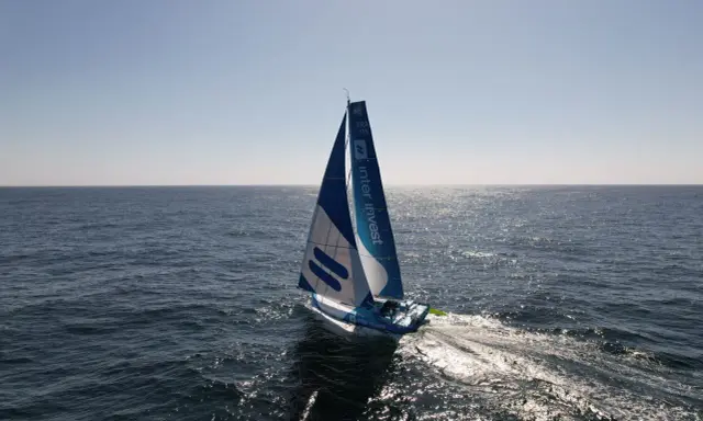 Voilier bleu et blanc "Inter Invest" naviguant sur une mer calme. Matthieu Perraut, skipper, est à la barre.