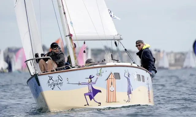 Un bateau muscadet décoré de personnages fantaisistes navigue sur l'eau, avec deux hommes à bord.