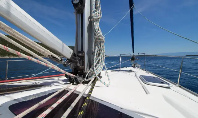 Vue de l'avant d'un voilier naviguant sur une mer bleue. Les cordages sont bien rangés, prêts à hisser le grand mât.