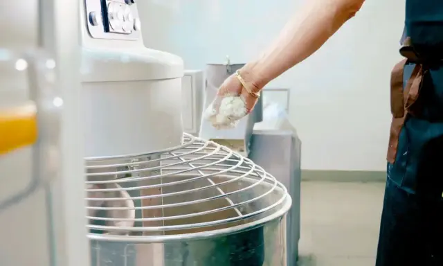 Main d'un boulanger ajoutant de la pâte à un pétrin, partie intégrante de l'entretien du matériel en cuisine.
