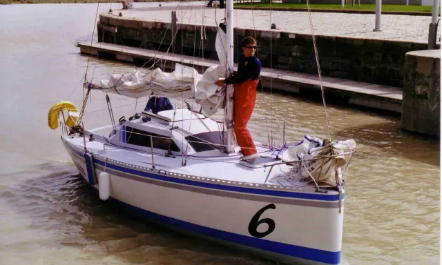 Un homme en salopette rouge prépare un voilier coco, le numéro 6 bien visible sur la proue, prêt à naviguer sur un canal.