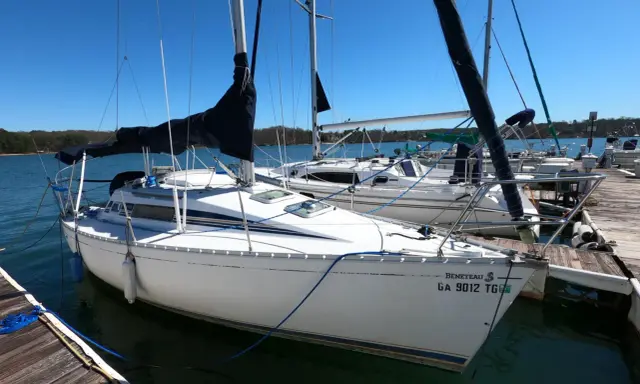 Voilier Beneteau First 235 blanc amarré à un ponton en bois, avec voiles noires et bleues.
