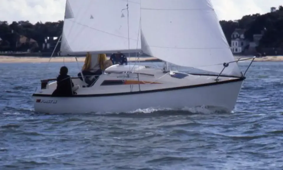 Voilier blanc naviguant sur une mer agitée, avec deux personnes à bord. Les premiers 18 avis sur ce modèle de bateau sont positifs.