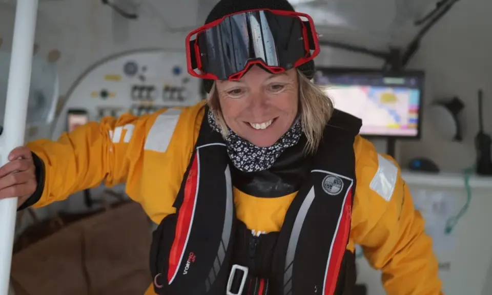 Alexia Barrier, souriante, porte une combinaison jaune et un gilet de sauvetage, prête pour une aventure maritime.