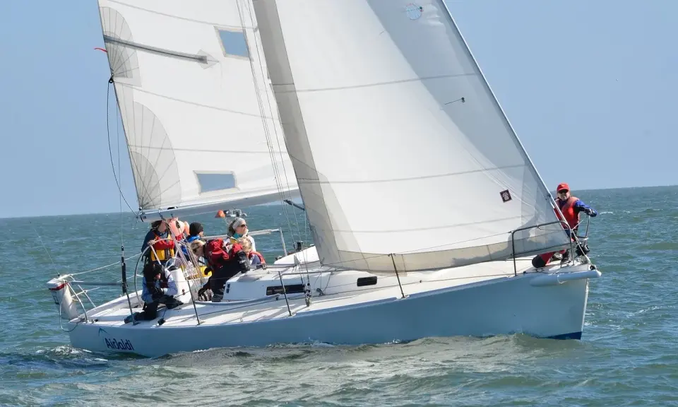 Équipage concentré sur un foc voilier blanc, naviguant sur une mer agitée sous un ciel bleu clair.