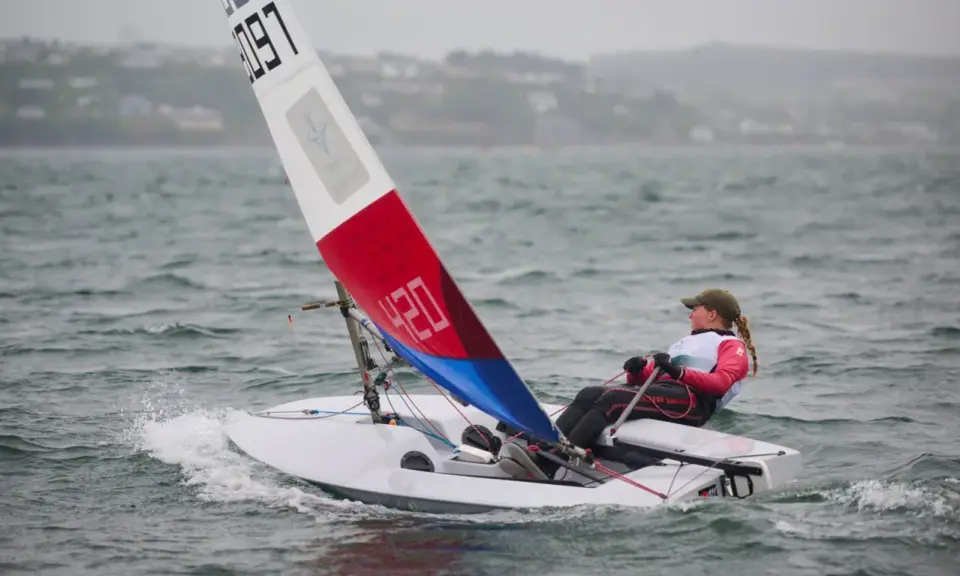 Jeune navigatrice en dériveur **tabur 320**, voile rouge et bleue, naviguant sur une mer agitée.