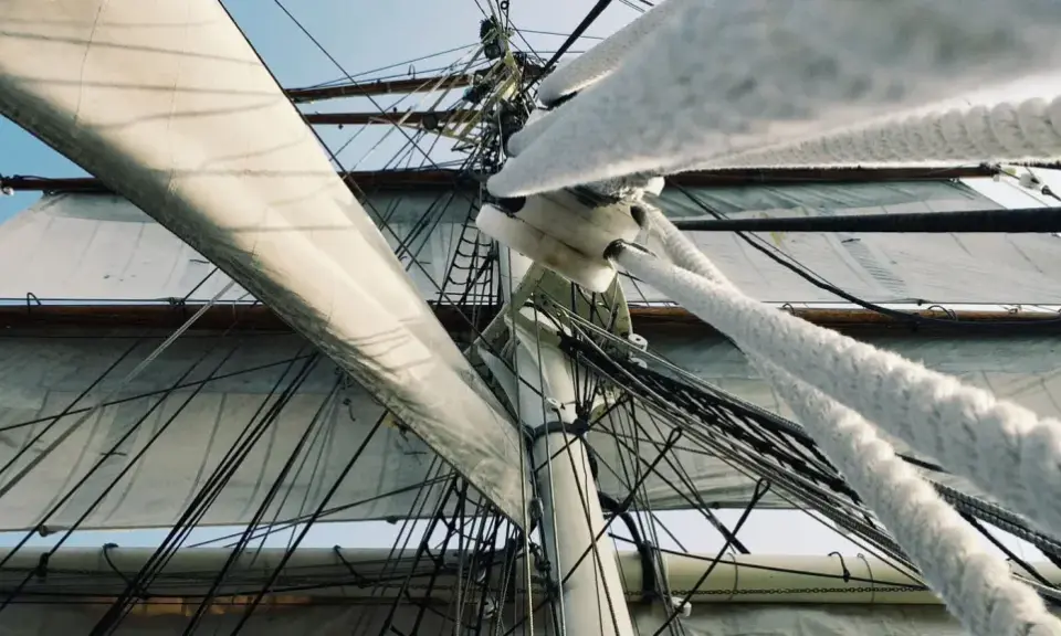Vue en contre-plongée des voiles d'un voilier, avec le gréement dormant complexe et les cordages épais.