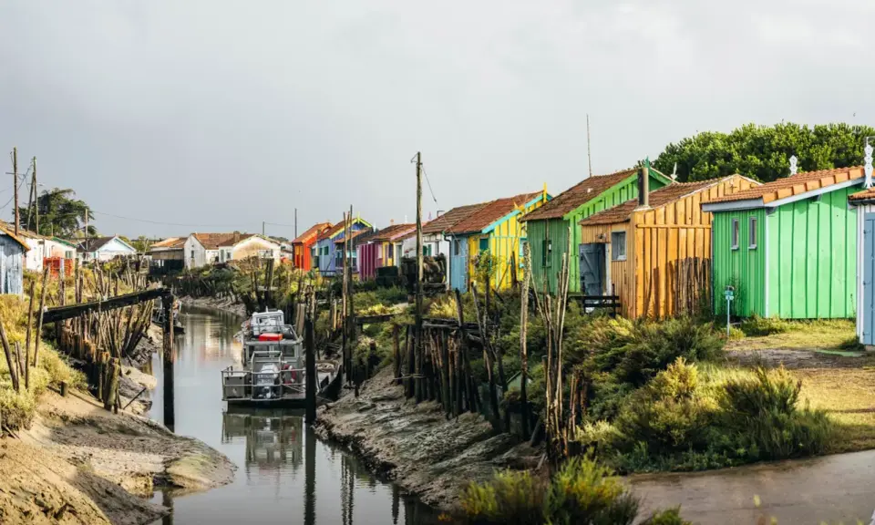 Cabanes colorées alignées le long d'un canal, un bateau amarré. Un charmant port sur l'Île d'Oléron.