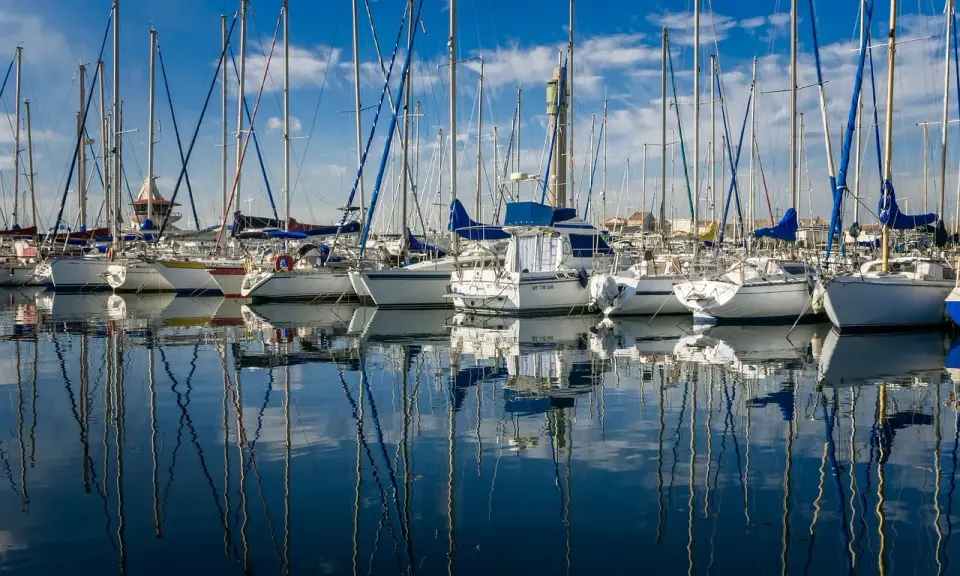 Une flotte de voiliers anglais, leurs mâts élancés se reflétant sur l'eau calme d'un port sous un ciel bleu éclatant.