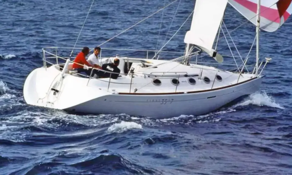 Voilier blanc naviguant sur une mer agitée. Trois personnes à bord. Le numéro 3517 est visible sur la coque.