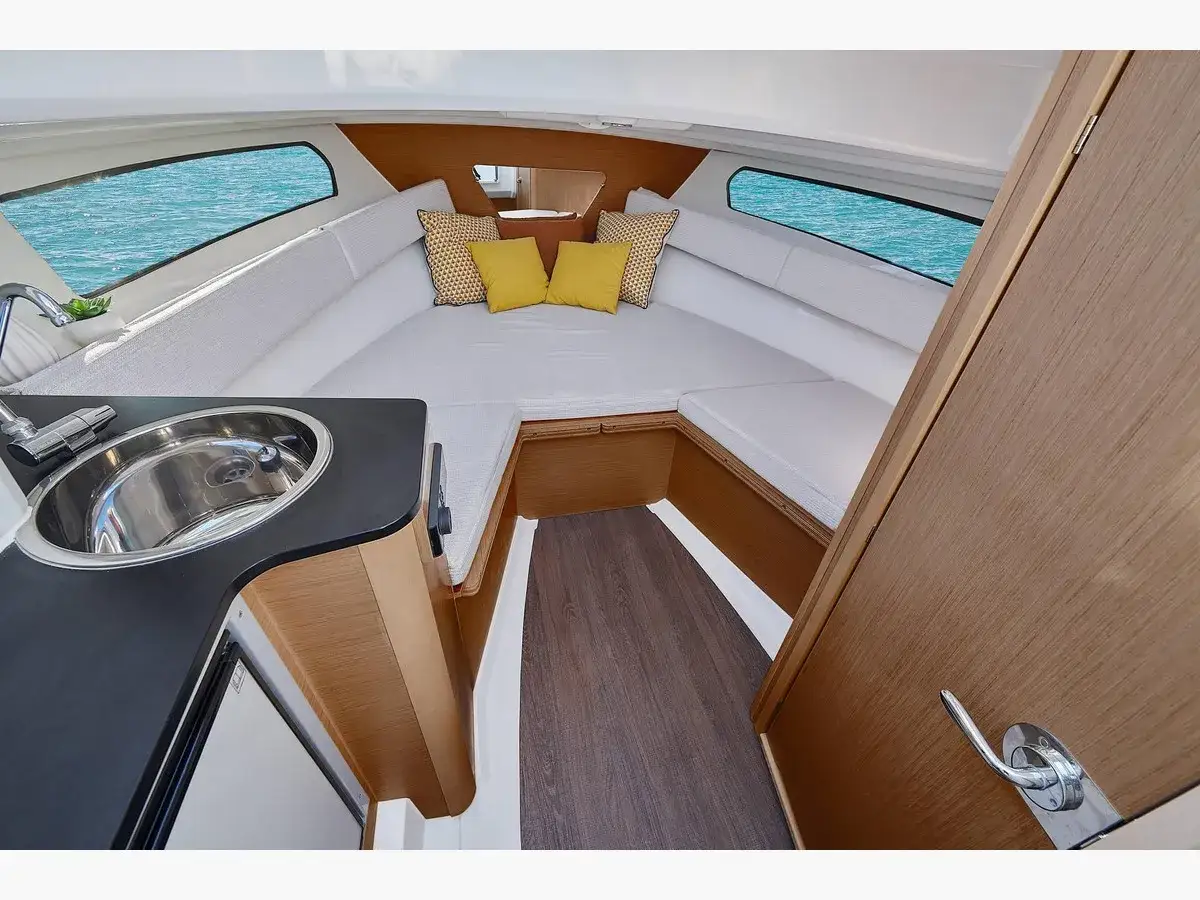 Intérieur du Sun Odyssey 24.1 : cabine confortable avec évier, banquettes et vue sur la mer bleue.