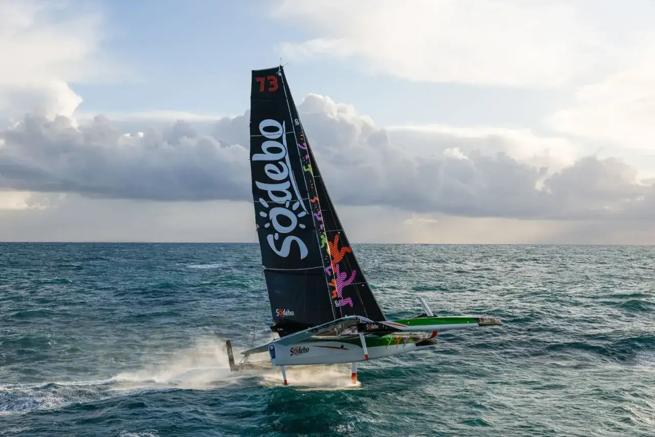 Le bateau de Thomas Coville, Sodebo Ultim 3, fend les vagues avec sa voile noire ornée de motifs colorés.