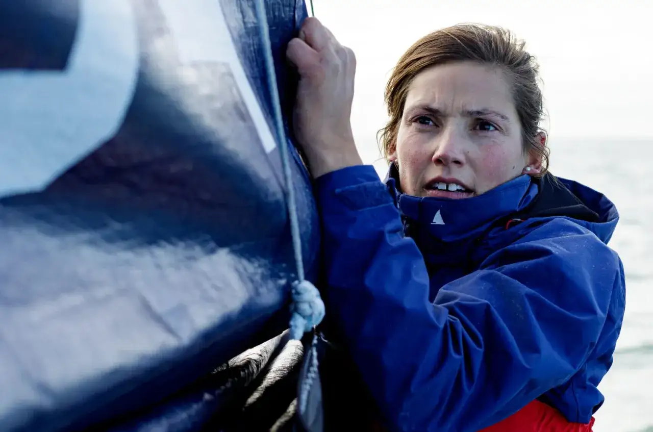 Tiphaine Ragueneau, concentrée, ajuste une voile bleue sur un bateau. La mer est calme.