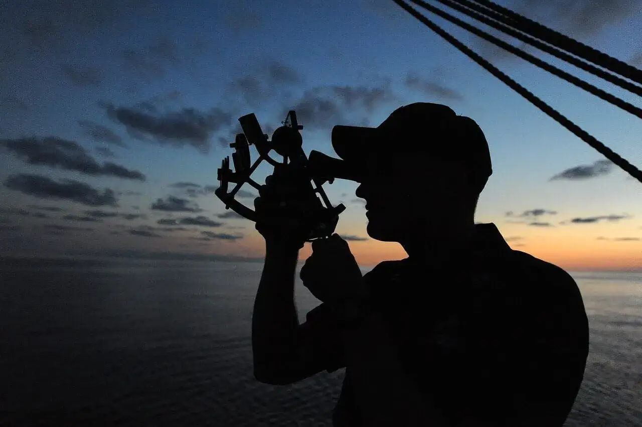Silhouette d'un marin utilisant un sextant pour la navigation au coucher du soleil.