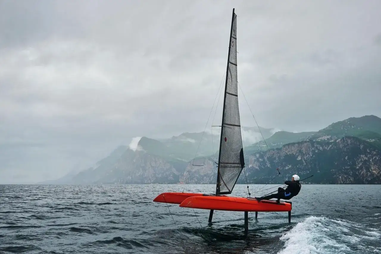Un voilier orange futuriste fend les vagues, ses foils hors de l'eau. Le marin, pench&eacute;, semble naviguer vers de nouveaux horizons, port&eacute; par les sails of change.