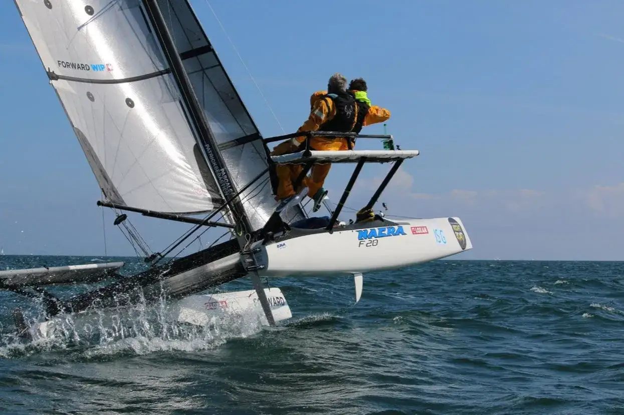 Le navigateur Yvan Bourgnon et un enfant sur un catamaran Naïra F20, naviguant sur une mer agitée sous un ciel bleu.