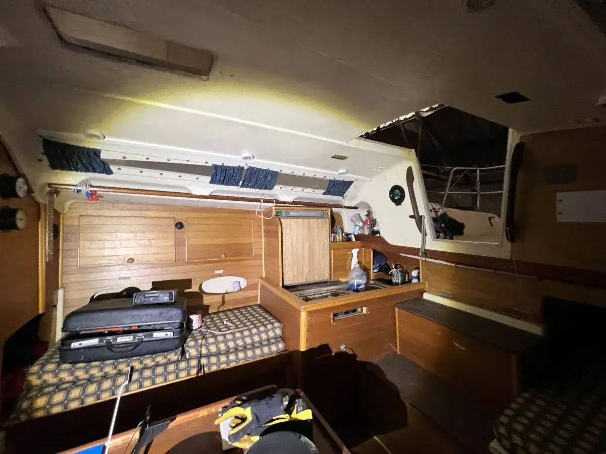 Intérieur d'un voilier Trident 80. Cabine avec banquette, placards en bois, et vue sur le cockpit.