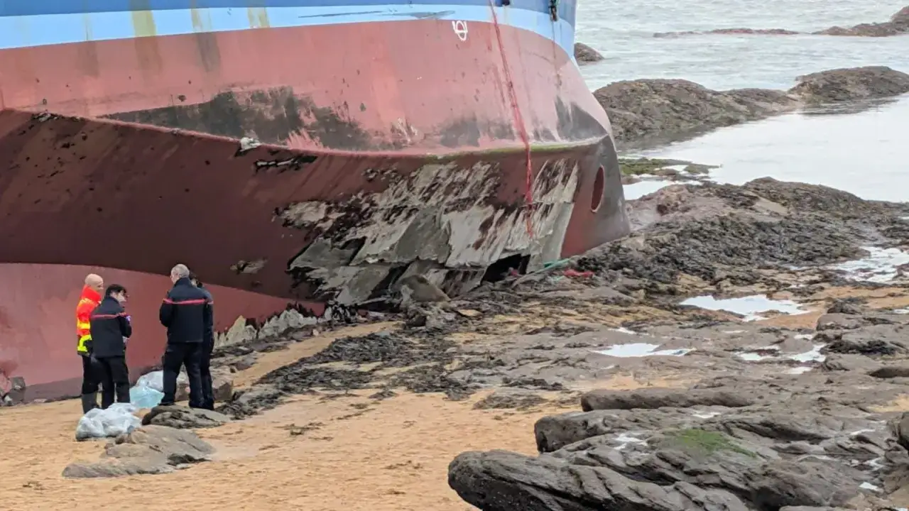 Trois pompiers inspectent le talonnage d'un bateau échoué sur des rochers, la coque endommagée.