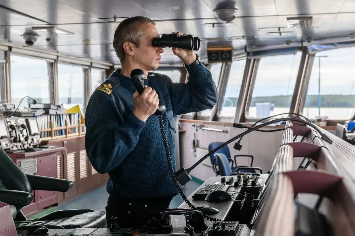 Le boat captain, jumelles à la main et téléphone à l'oreille, surveille l'horizon depuis la passerelle.