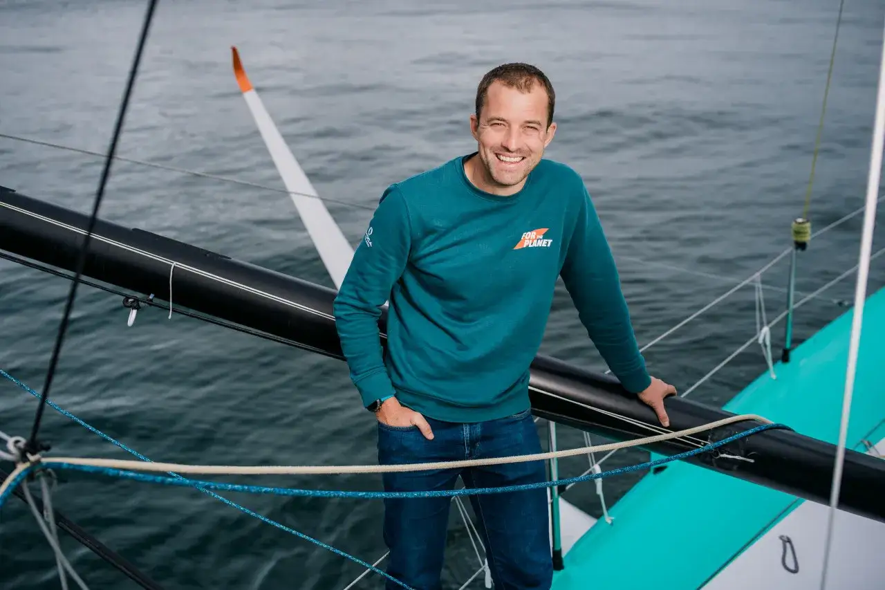 Sam Goodchild, skipper souriant sur un voilier, porte un sweat 