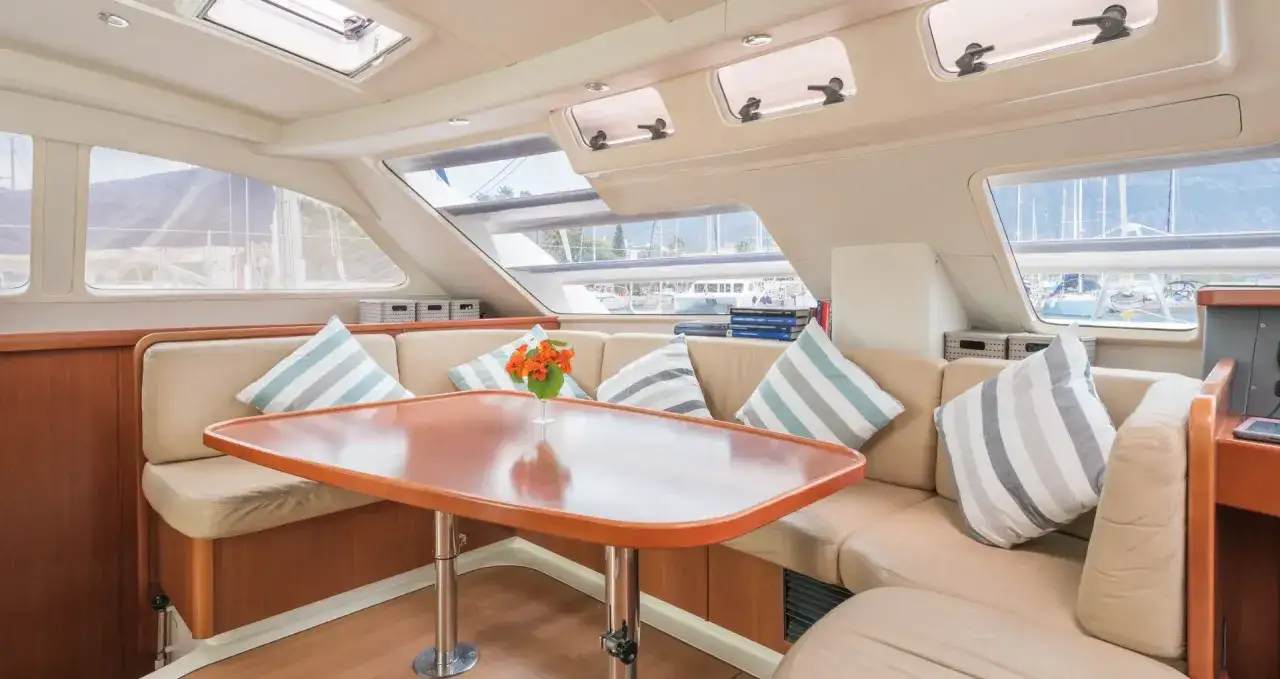 L'élégant intérieur d'un voilier 8m offre un espace de vie confortable avec des banquettes en cuir clair, des coussins rayés et une table en bois.