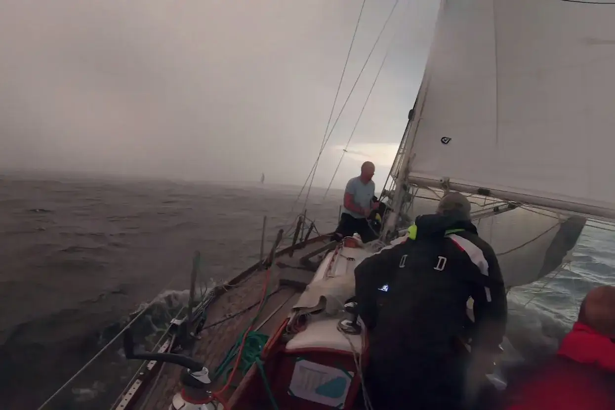 Un voilier affronte une tempête, les vagues déferlent et la visibilité est réduite par le brouillard. L'équipage lutte pour garder le contrôle.