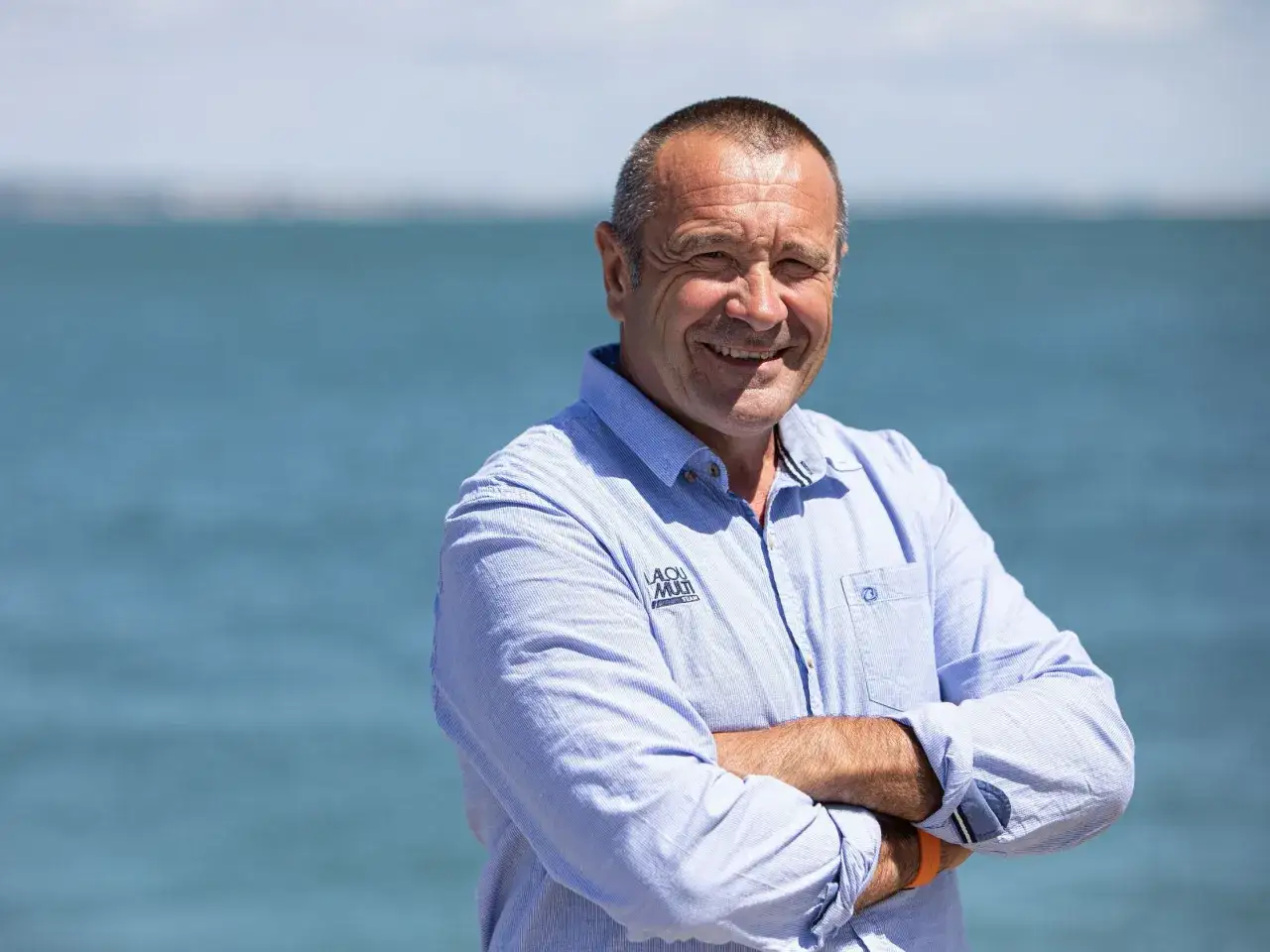 Lalou Roucayrol, un homme souriant, bras croisés, devant la mer.