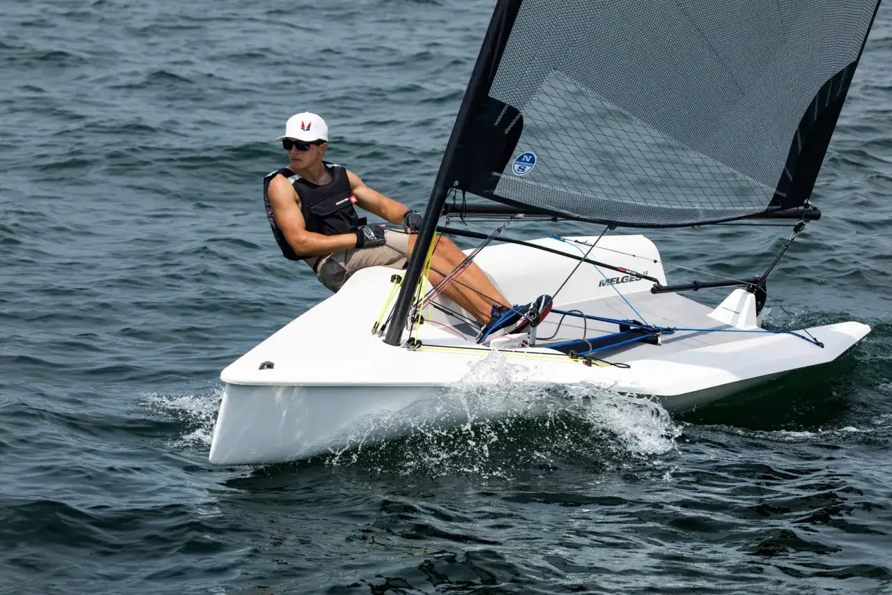 Un jeune homme navigue en deriveur solo, le bateau fend les vagues dans un sillage écumeux.
