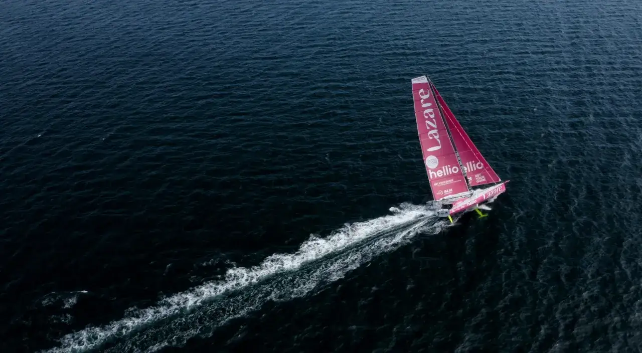 Voilier IMOCA Lazare fendant les vagues, laissant une traînée blanche derrière lui.