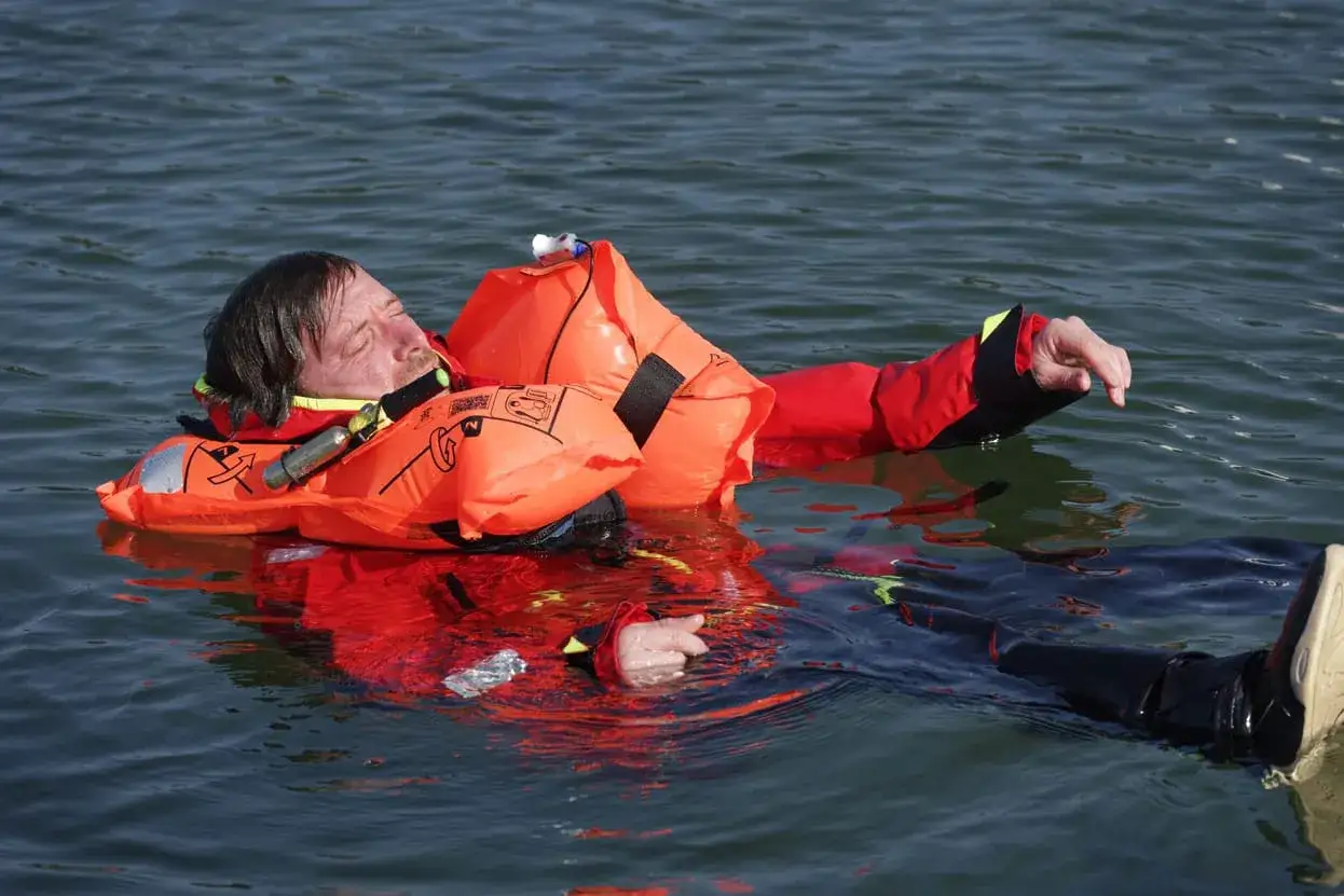 Un homme en gilet de sauvetage orange flotte dans l'eau, survivant d'un naufrage de bateau.