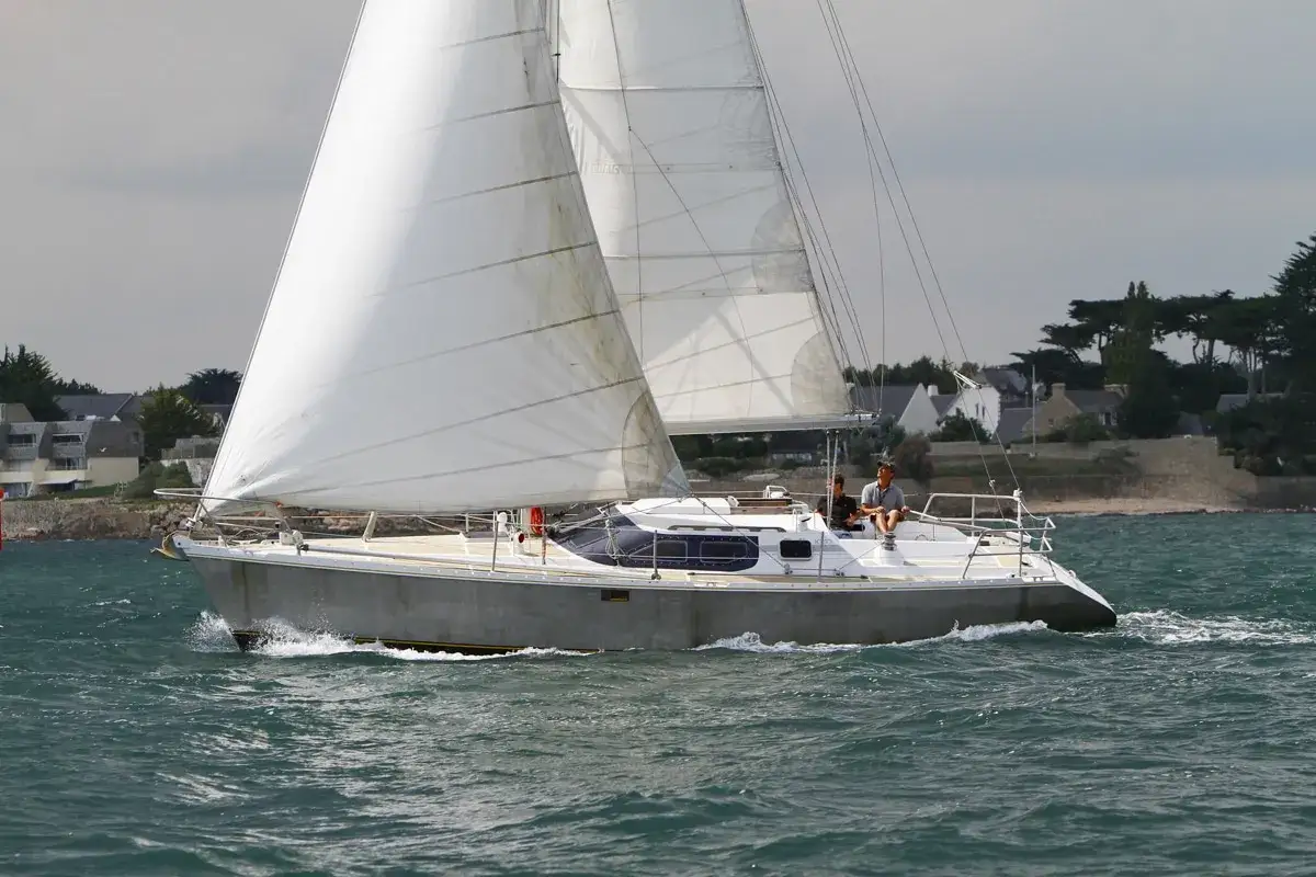 Un voilier Jurançon navigue sur une mer agitée, deux personnes à bord profitent de la brise.