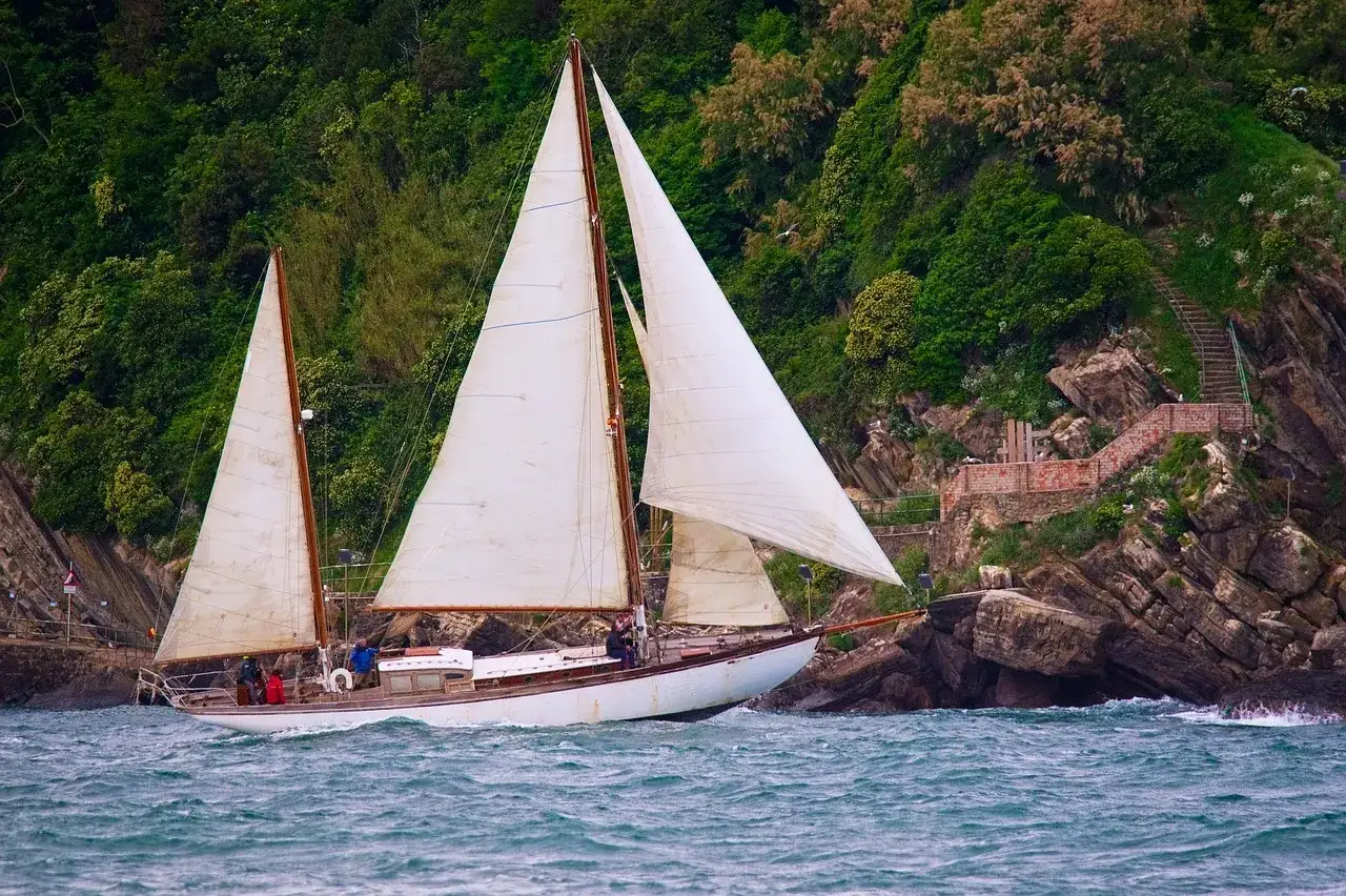 Un magnifique voilier 2 mâts navigue près d'une côte rocheuse verdoyante. Les voiles blanches gonflées par le vent donnent une impression de liberté.