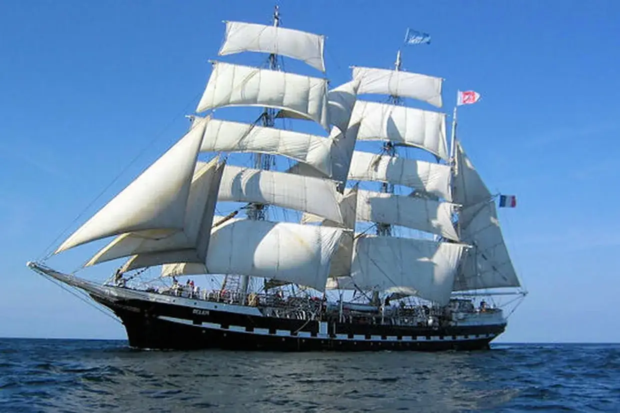 Le majestueux bateau Belem, un trois-mâts historique, navigue fièrement sous un ciel bleu, ses voiles blanches gonflées par le vent.