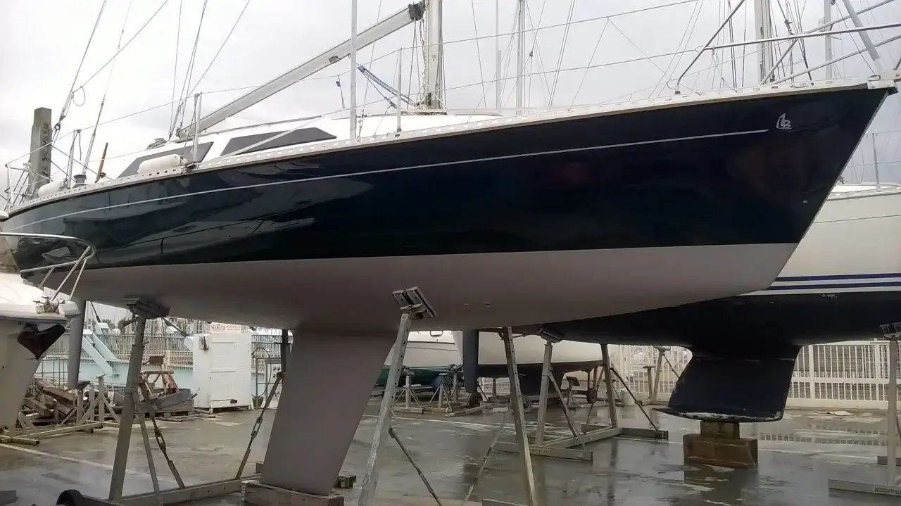 Un voilier suspendu sur des chandelles, prêt pour l'hivernage. Sa coque sombre et sa quille grise annoncent de futures aventures nautiques.