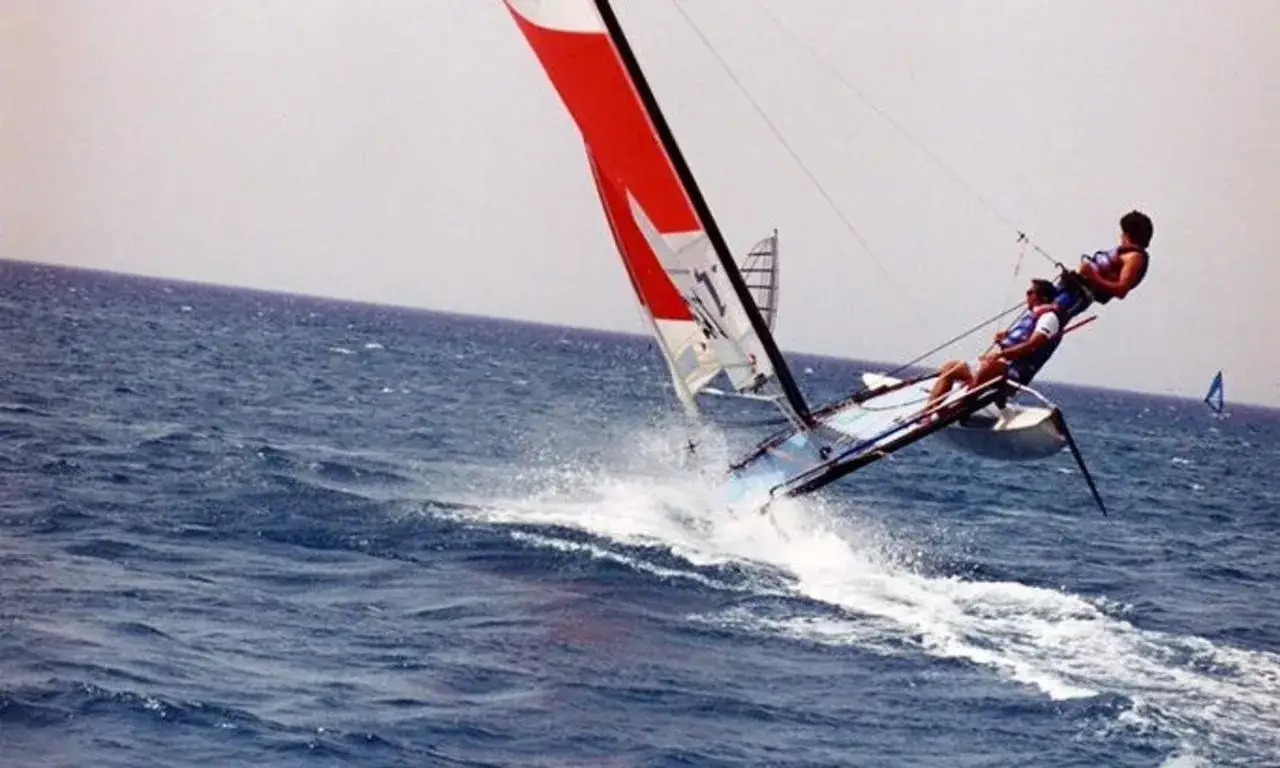 Deux personnes naviguent sur un Hobie Cat 16, le catamaran est en plein vol, créant des gerbes d'eau. Fiche technique du Hobie Cat 16.