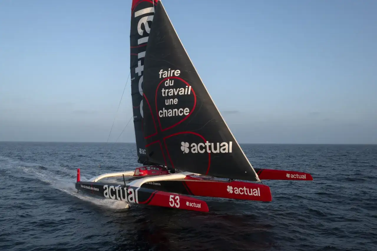 Trimaran de course Actual, sponsorisé par Franck Cammas, naviguant sur une mer calme sous un ciel bleu.