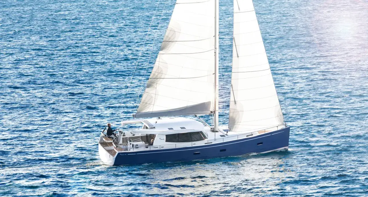 Un voilier bleu et blanc, un Sirius 40 DS, navigue sur une mer bleue étincelante, ses voiles gonflées par le vent.